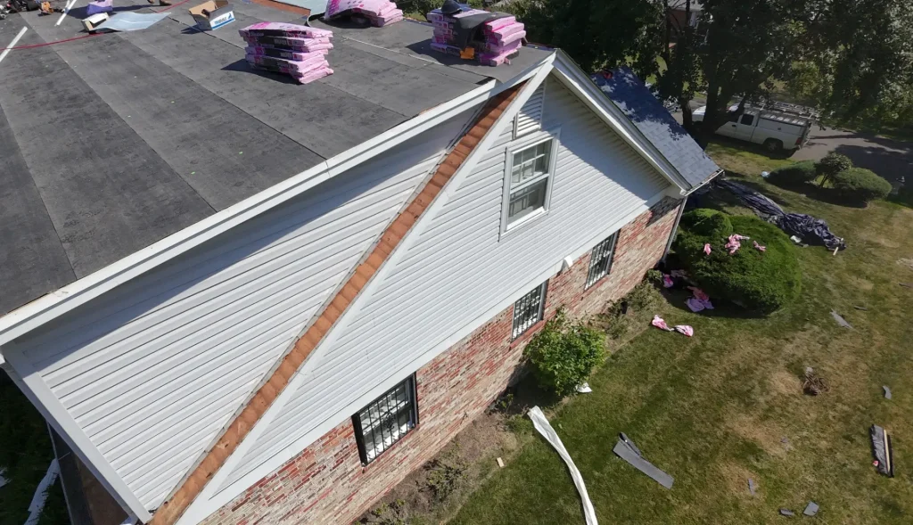 Aerial view of a house with a dark roof under construction, pink roof insulation, and white siding.